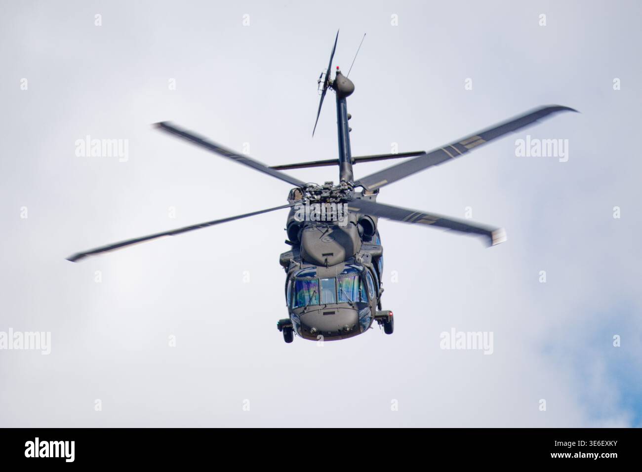 Un elicottero militare scuro con le sue lame principali del rotore sfocate in movimento vola in alto contro un cielo luminoso e nuvoloso. Foto Stock