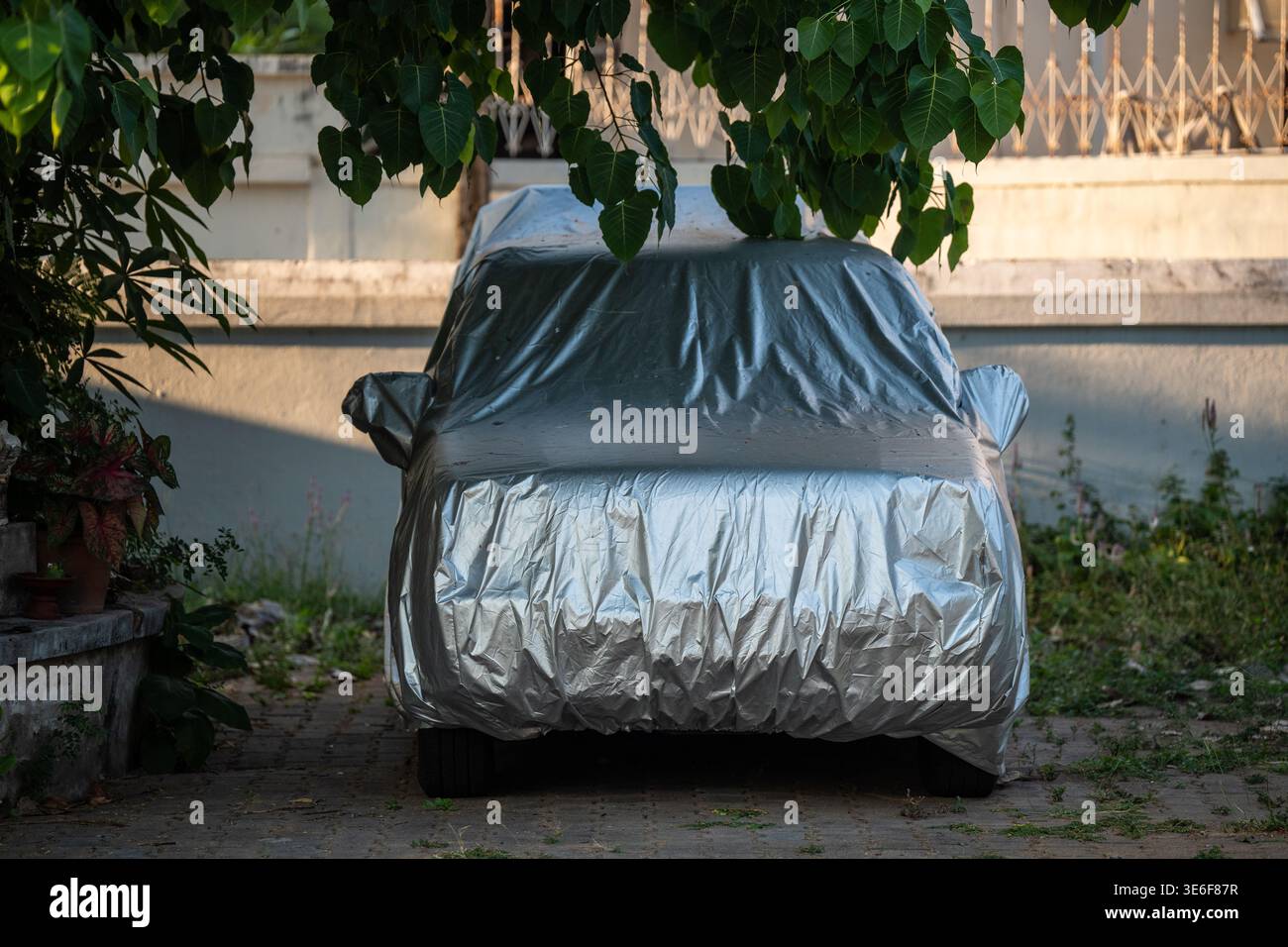 Auto coperta con copertura contro il sole e riscaldamento parcheggiata all'ombra sotto l'albero nelle calde giornate estive in città. Foto Stock