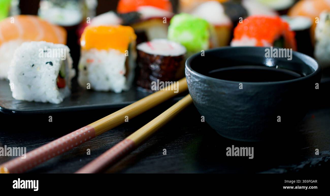Piatto di sushi con vari tipi di sushi e una ciotola di salsa di soia su un tavolo scuro Foto Stock