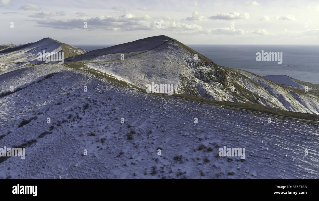 Luftaufnahme von verschneiten Felsen, blaues Meer, auf bewoelktem Himmel Hintergrund. Aufnahme. Schneebedeckten Huegeln sull'isola am Meer in einem Win Foto Stock