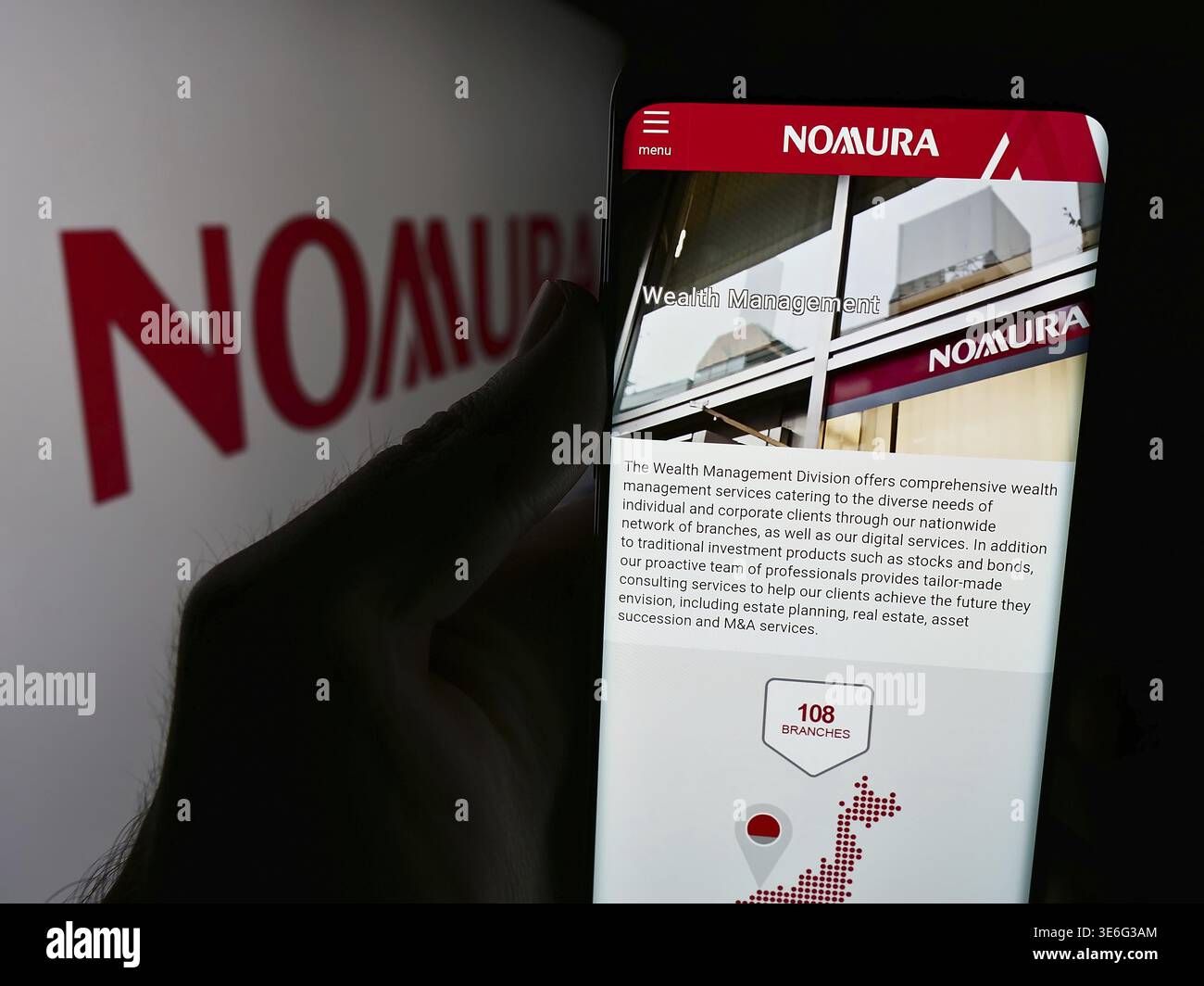 Stoccarda, Germania - 08-12-2024: Persona che detiene il cellulare con il sito web della società giapponese di servizi finanziari Nomura Holdings Inc. Con il logo. Concentrati su Foto Stock