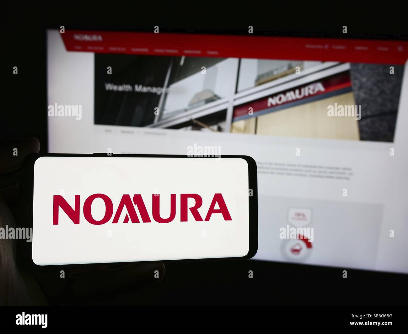 Stoccarda, Germania - 12-08-2024: Persona che detiene uno smartphone con logo della società giapponese di servizi finanziari Nomura Holdings Inc. Davanti al sito web. Foto Stock