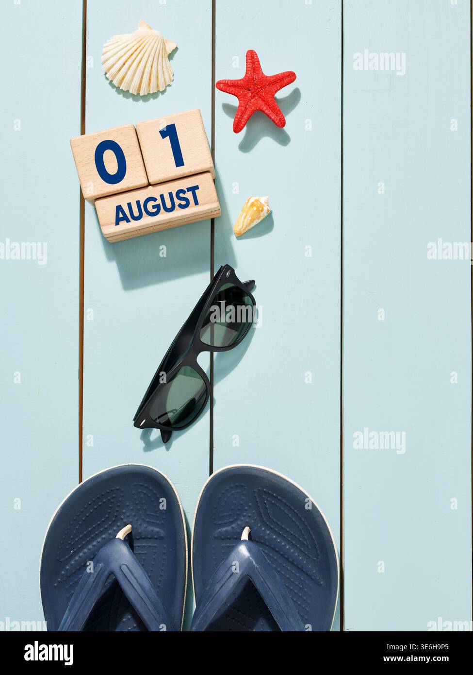 Composizione estiva fatta di accessori da spiaggia e calendario a blocchi di legno che mostra il 1° agosto, evocando il concetto di vacanza estiva Foto Stock