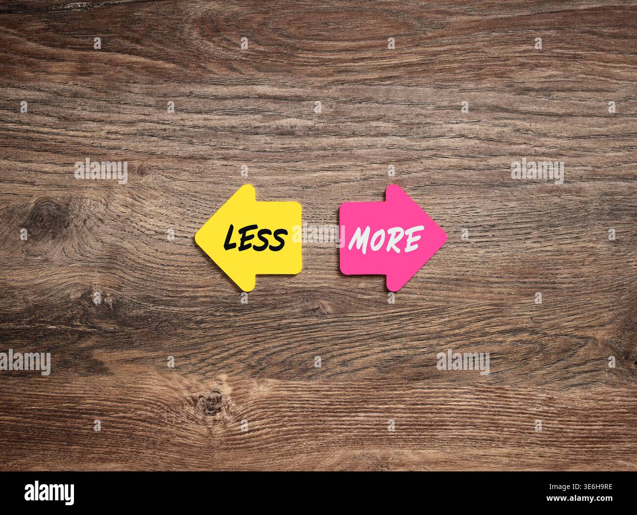Due frecce opposte che puntano in modi diversi con meno o più scritte su di esse, posizionate su una scrivania di legno, che rappresentano lo stile di vita minimalista rispetto al consu Foto Stock