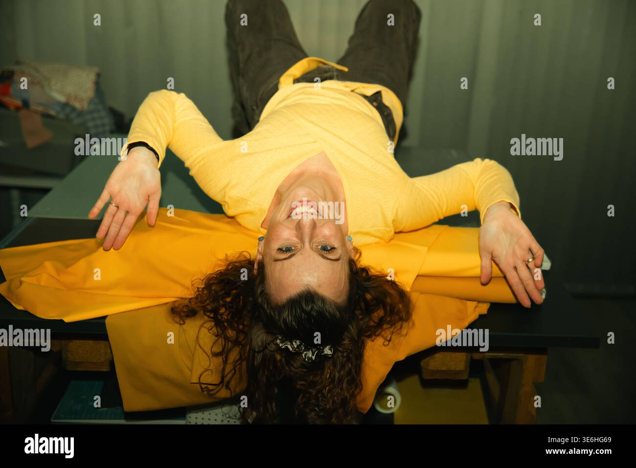 Donna adulta caucasica con gioia sdraiata a testa in giù sul tavolo con un vestito giallo. Foto Stock