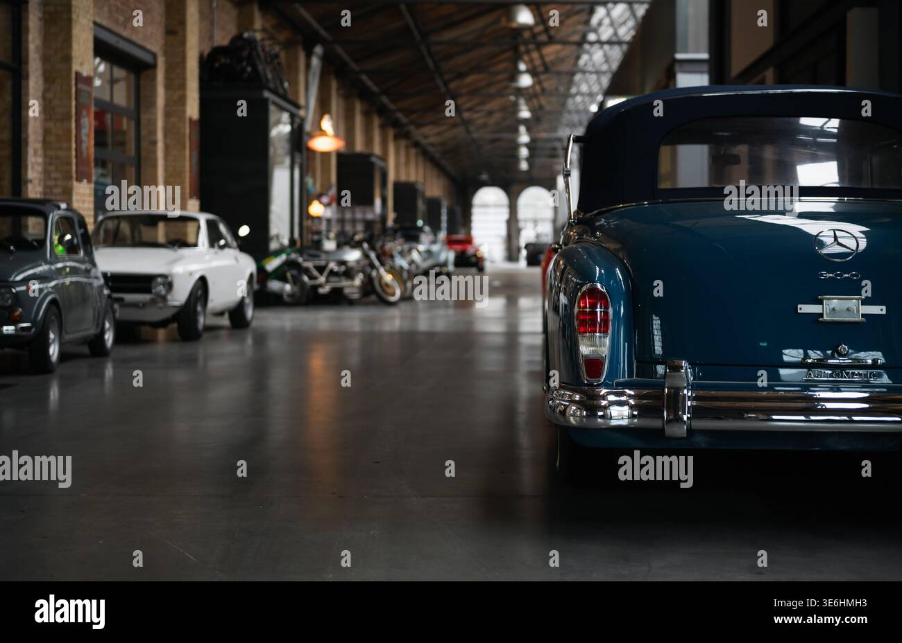 Mercedes-Benz 300 Adenauer blu in corridoio scuro. Vista posteriore della classica Mercedes decappottabile parcheggiata tra le altre vecchie auto nel corridoio industriale. Foto Stock