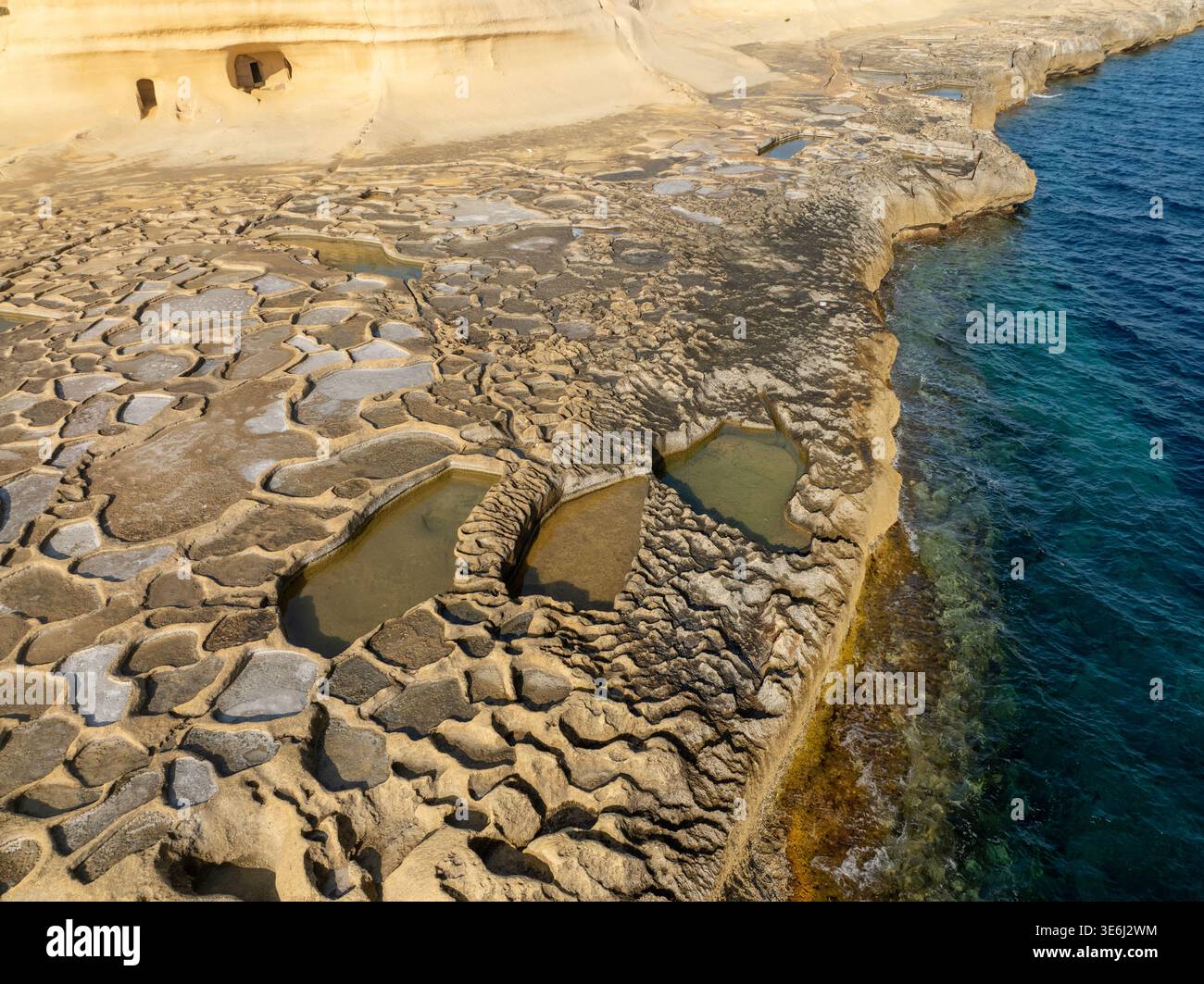Vista aerea delle saline geometriche scolpite nella roccia dorata, che riflette il cielo, incontra il mare blu profondo, Gozo, Malta. Foto Stock