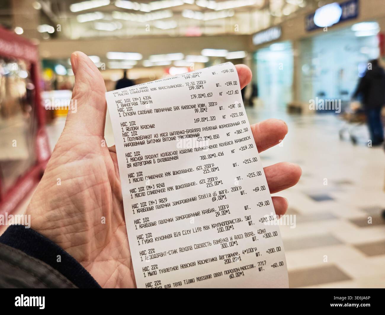 Kirov, Russia - 8 febbraio 2026: Un cliente possiede una ricevuta del negozio con i dettagli degli acquisti recenti in un supermercato affollato. La ricevuta mostra gli articoli bo Foto Stock