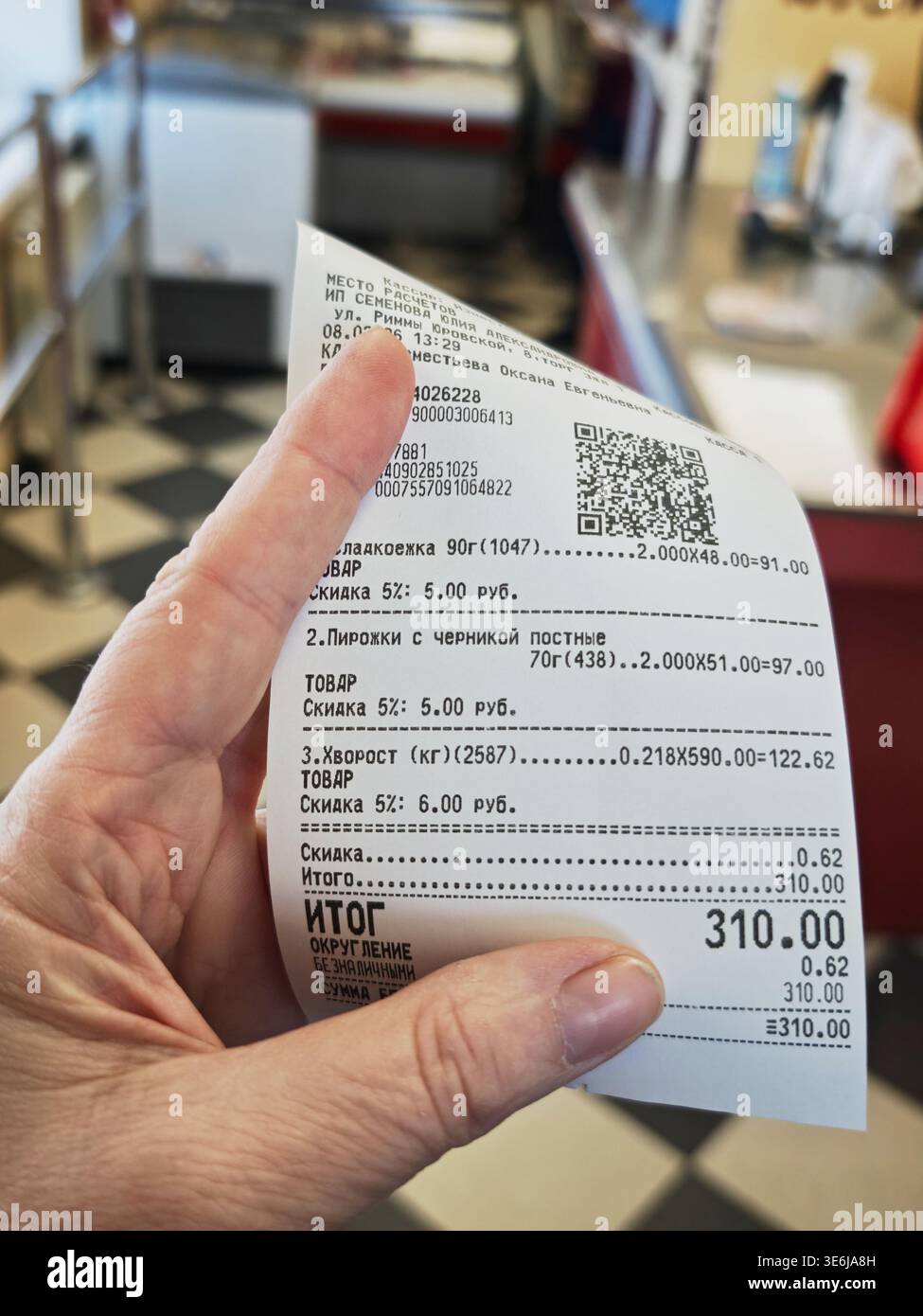 Kirov, Russia - 8 febbraio 2026: La mano tiene in mano una ricevuta del negozio con il costo totale dopo lo shopping. La ricevuta elenca gli articoli acquistati, gli sconti applicati, un Foto Stock