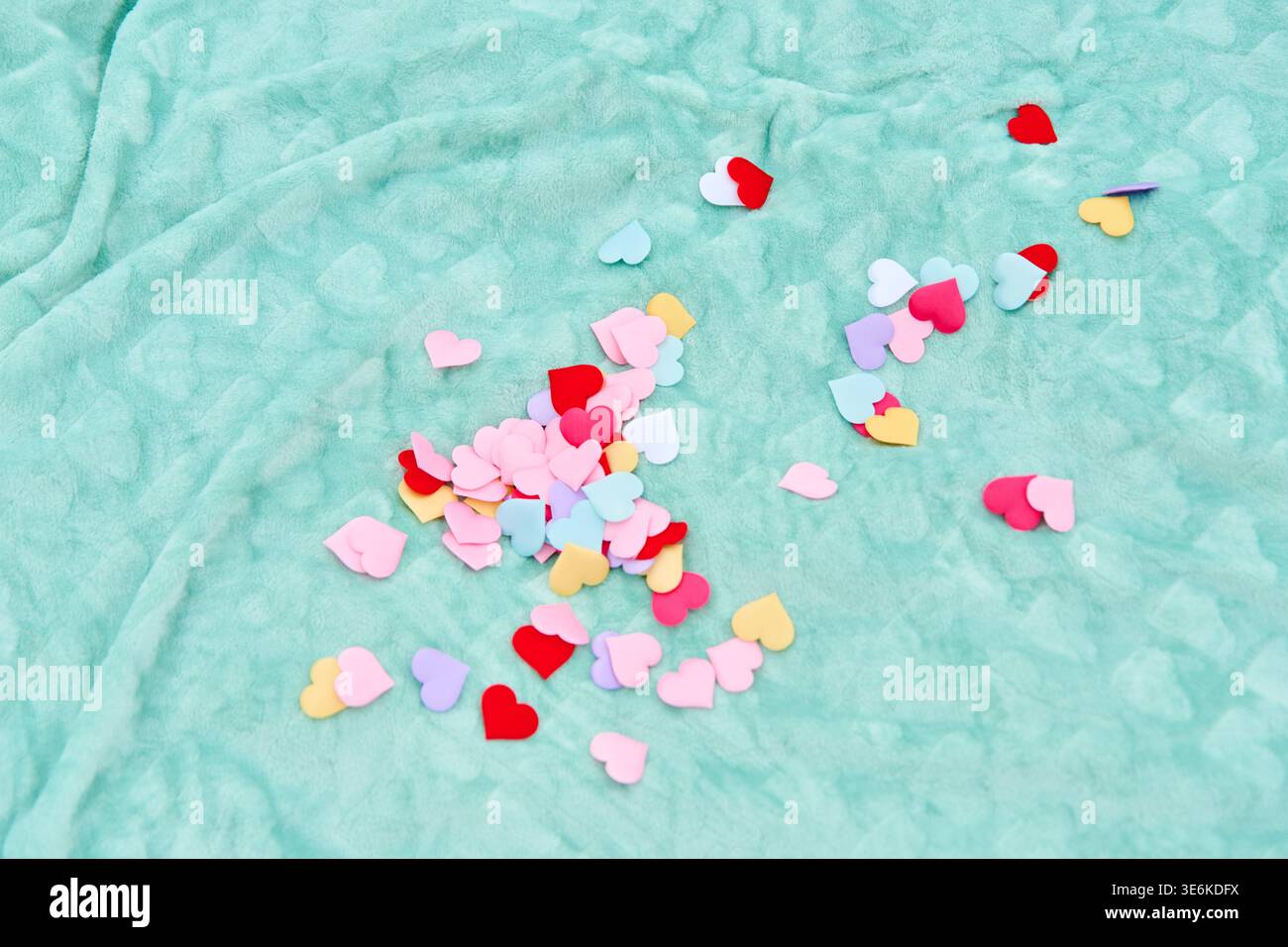 Vari piccoli cuori di carta in rosso, rosa, viola, giallo e bianco sparsi casualmente su tessuto increspato blu chiaro, evocando temi d'amore Foto Stock