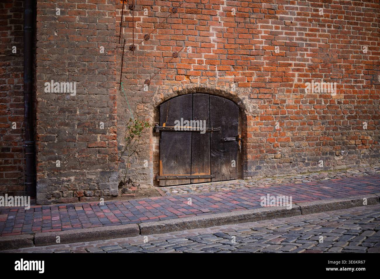 Una porta in legno con cerniere in ferro è annidata in un edificio in mattoni rossi Foto Stock