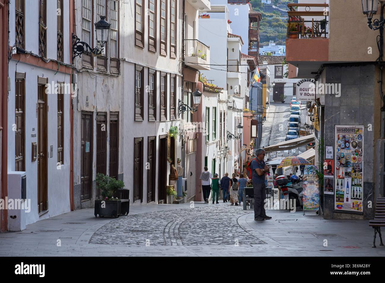 ICOD DE LOS VINOS, TENERIFE, SPAGNA – 4 GIUGNO 2025: Pedoni che passeggiano lungo una strada acciottolata nel centro storico di Icod de los Vinos, fiancheggiata Foto Stock
