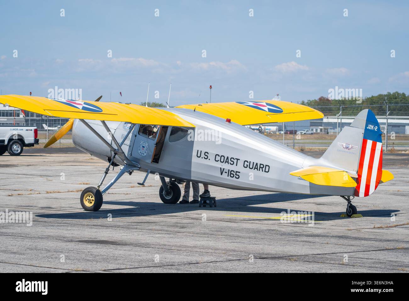 Un velivolo vintage monomotore della Guardia Costiera degli Stati Uniti con ali gialle luminose parcheggiato su un grembiule aeroportuale, che mostra segni storici e pattuglia marittima Foto Stock