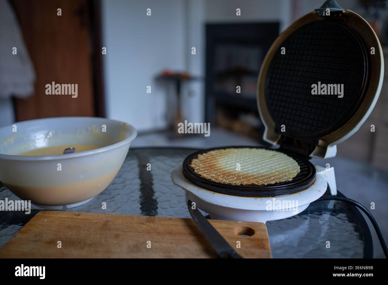 Mini ferro da stiro per preparare l'impasto per pancake su un tavolo di vetro, recipiente per mescolare con l'impasto rimanente e coltello su legno Foto Stock