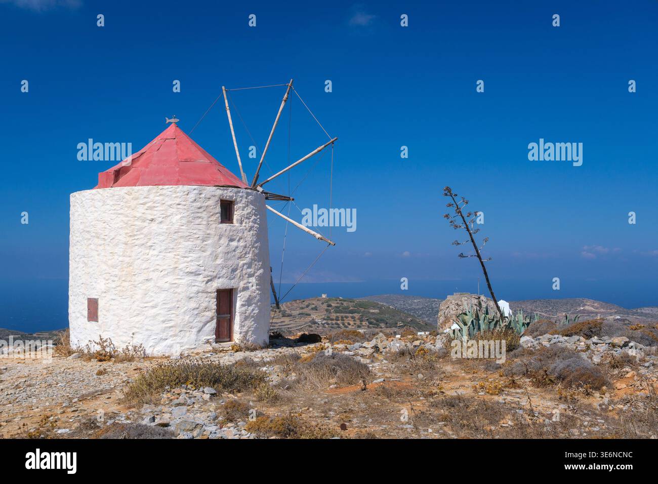 Mulino a vento con tetto rosso e vele in legno sulla collina che si affaccia sul mare Foto Stock