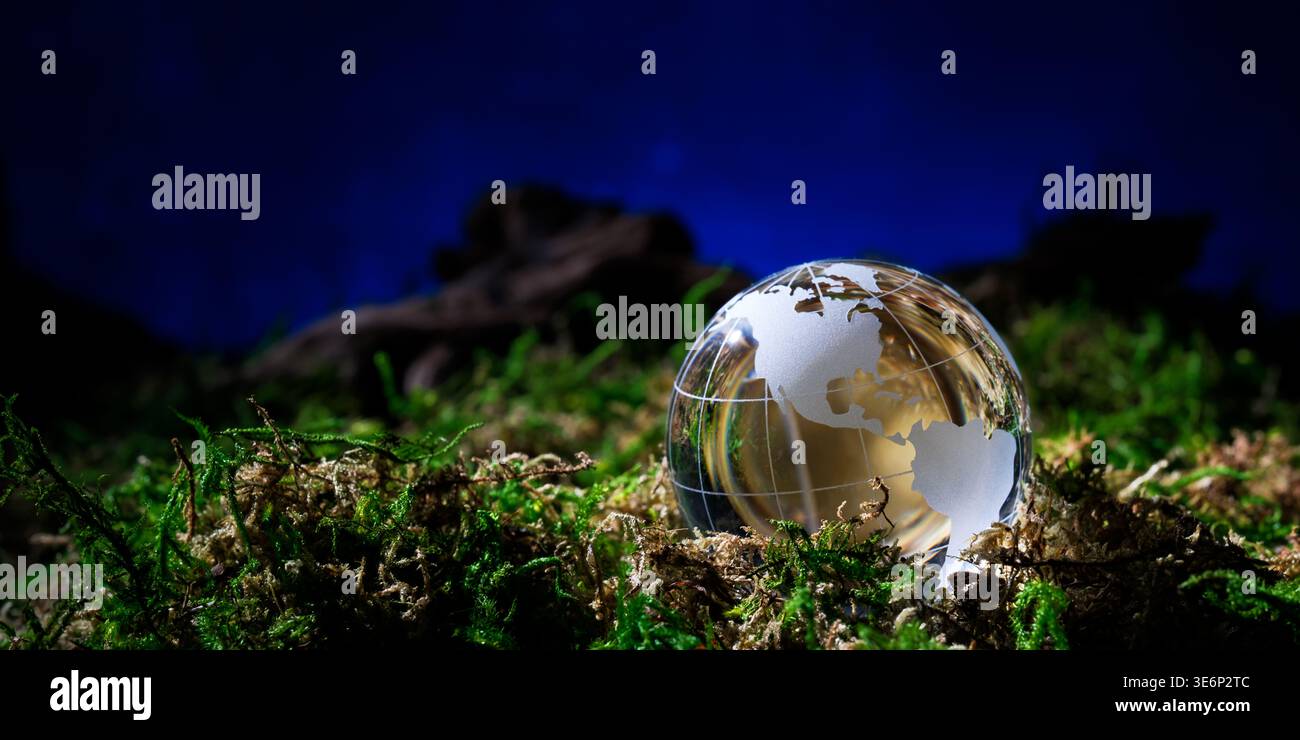 Globo in vetro con le Americhe che riposano nel muschio sotto uno sfondo blu profondo, simboleggiando la sostenibilità ambientale e la consapevolezza del clima globale Foto Stock