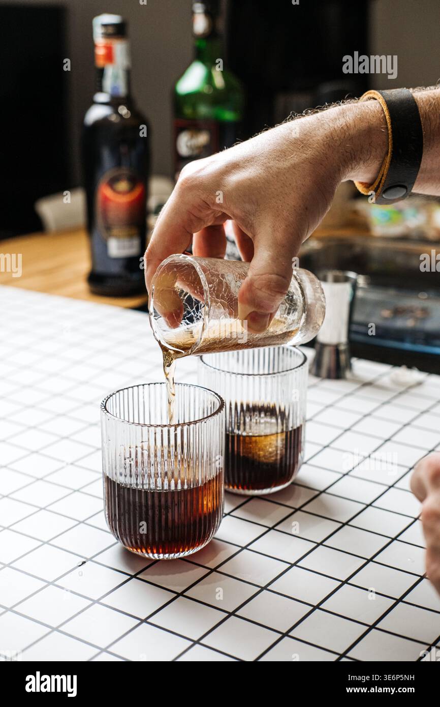 Due bicchieri con liquido scuro e ghiaccio accanto alle bottiglie Cynar e Borghetti. Liquori botanici consumo consapevole alternativo di cocktail, salute Foto Stock