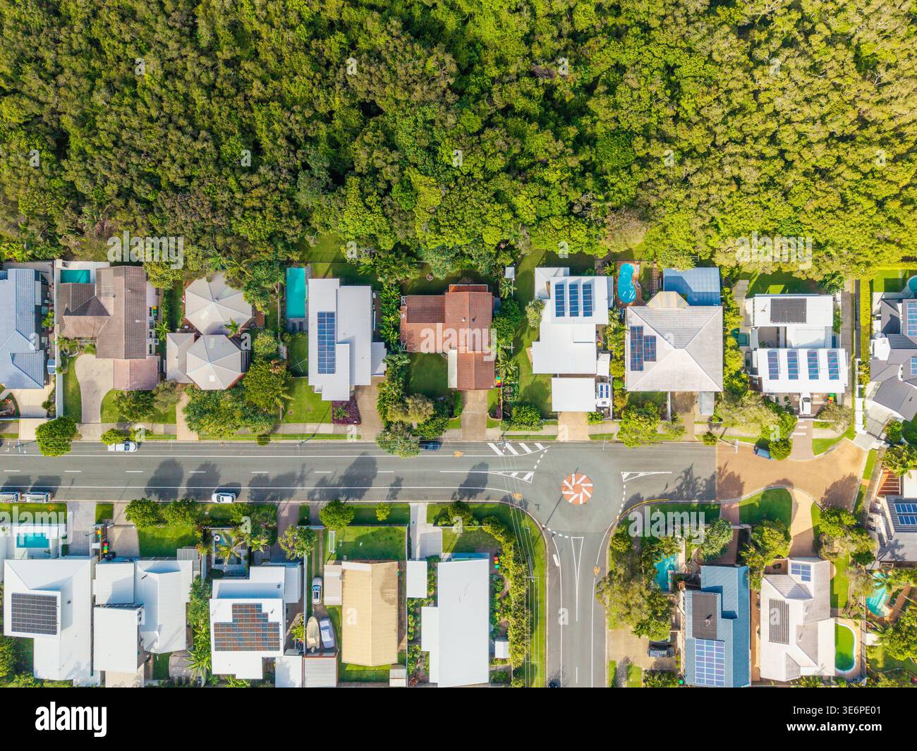 Un colpo di droni in testa cattura una vivace area suburbana nel Queensland, mostrando case, strade, piscine e pannelli solari adiacenti a un denso for Foto Stock