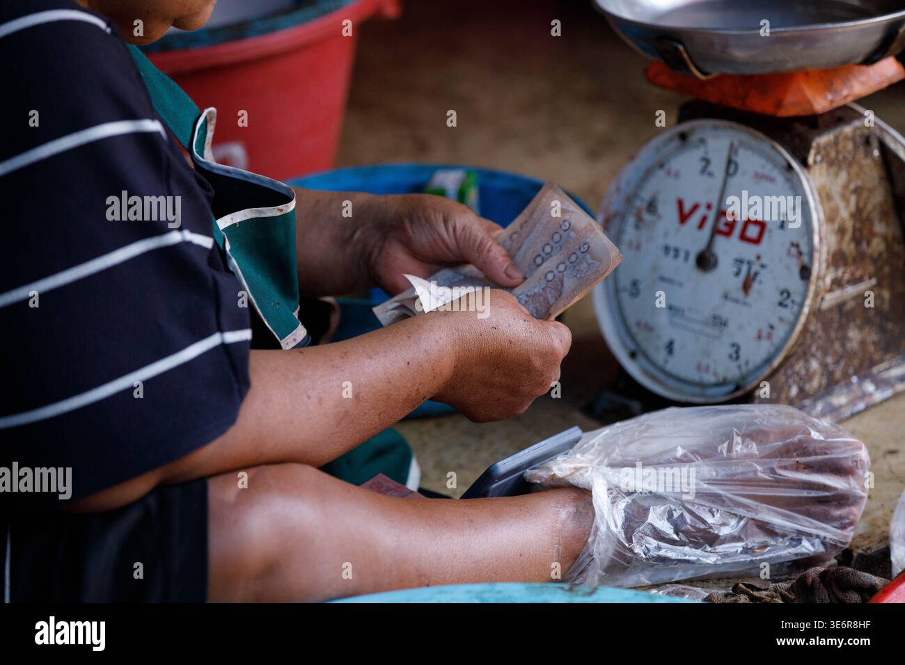 SAMUT SONGKHRAM, THAILAND-Mar 28, 2026: Hands of fish market vendor counting banconote, Cultural Street market commerce in Asia, close up, a Maeklong Foto Stock