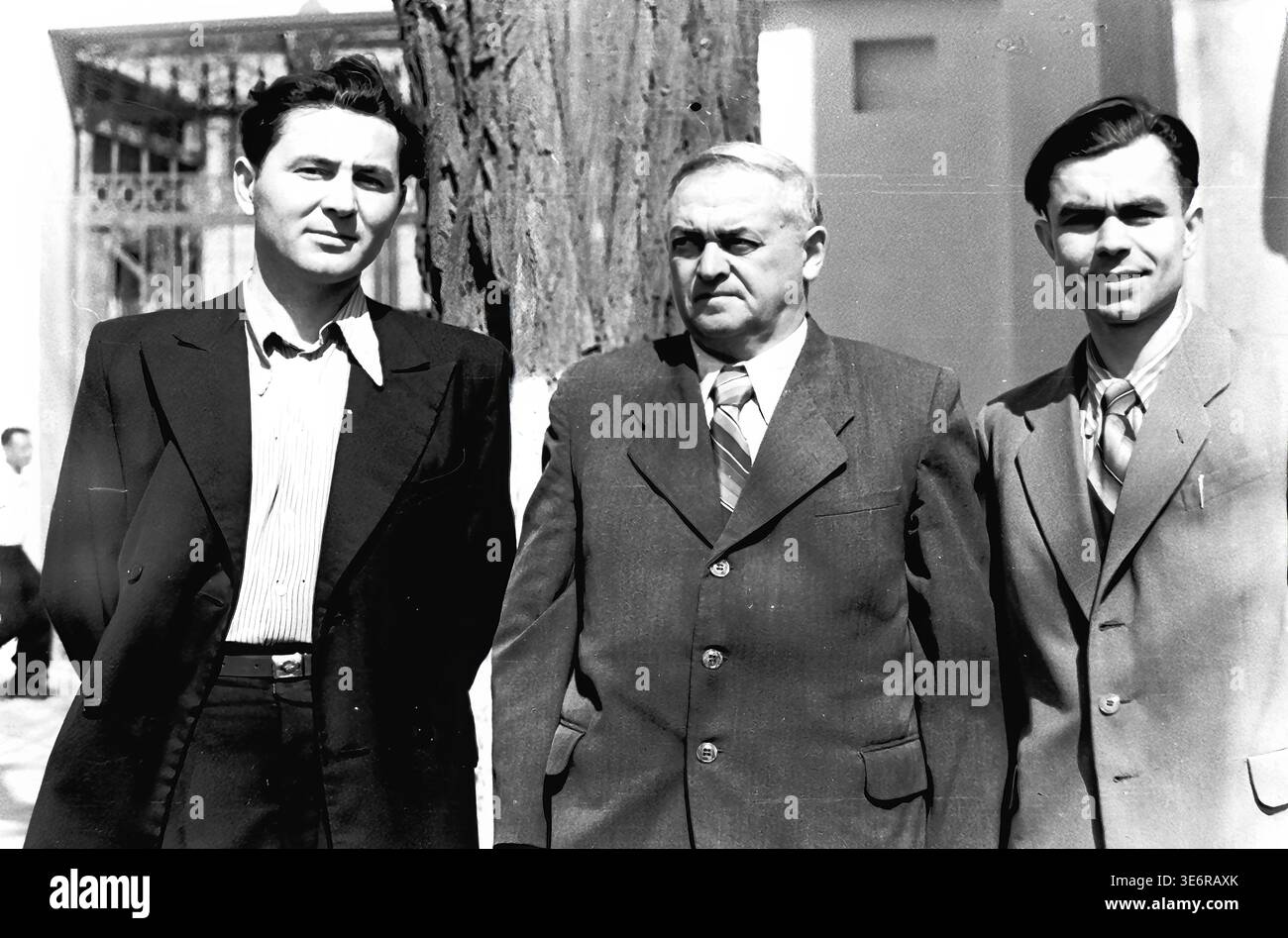 Sloviansk, 1950 anni. All'esterno dell'impianto di armatura e isolamento (AIZ). Tre fiduciosi uomini sovietici vestiti con abiti formali affilati posano insieme accanto a un tronco di albero grezzo nel cortile della fabbrica. I colleghi attendono con calma l'inizio di una manifestazione di massa festosa in una giornata molto luminosa e soleggiata. Questa fotografia d'archivio in bianco e nero altamente autentica mostra splendidamente la moda maschile della metà del secolo, le forti amicizie professionali, l'amministrazione della fabbrica e il ricco patrimonio culturale del pacifico Donbas. Foto Stock
