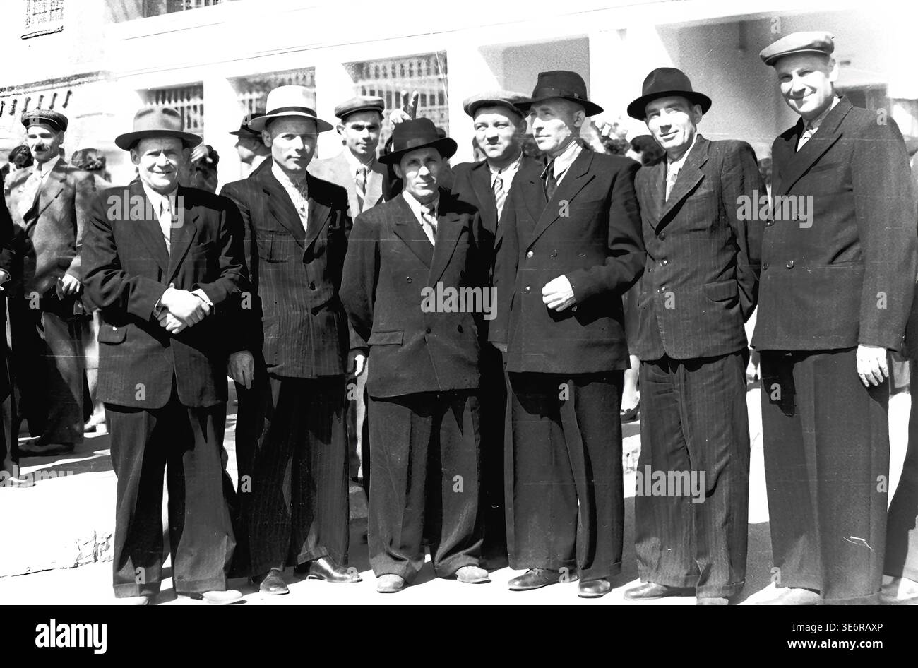 Sloviansk, 1950 anni. Il territorio dell'impianto di armatura e isolamento (AIZ). Un grande gruppo di sette dirigenti di fabbrica sovietici e ingegneri senior è orgoglioso di trovarsi in una lunga fila fuori da un edificio bianco. Gli uomini rispettabili indossano abiti formali, cappotti scuri e cappelli eleganti mentre si riuniscono per una manifestazione di massa festosa. Questa fotografia d'archivio espressiva in bianco e nero documenta perfettamente la leadership collettiva, la classica moda all'aperto della metà del secolo, gli eventi della comunità e la memoria storica duratura del pacifico Donbas. Foto Stock