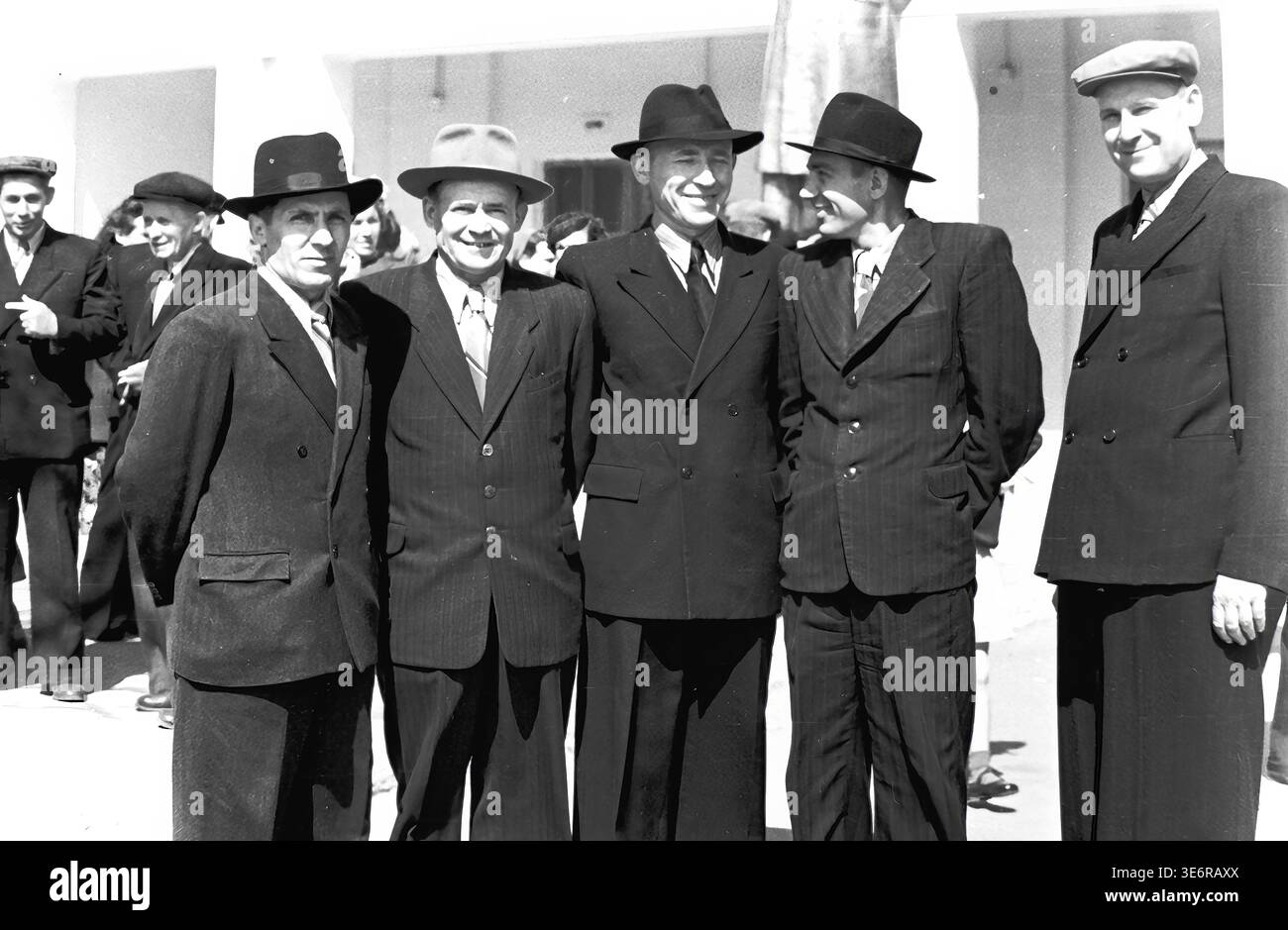 Sloviansk, 1950 anni. All'esterno dell'impianto di armatura e isolamento (AIZ). Sei allegri uomini sovietici in abbigliamento formale si riuniscono per scattare una foto di gruppo durante un evento all'aperto luminoso e soleggiato. Gli amministratori della fabbrica e i lavoratori senior indossano abiti classici e cappelli eleganti mentre si preparano per una dimostrazione di massa. Questa immagine d'archivio in bianco e nero altamente autentica riflette brillantemente autentiche relazioni sul posto di lavoro, la moda maschile vintage e la ricca atmosfera storica del tranquillo Donbas. Foto Stock