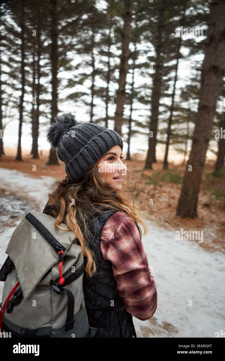 Pensiero, donna e trekking con sorriso in inverno, escursionismo e avventura sulla neve in vacanza nella foresta. Esterno, escursionista e persona con abiti caldi per Foto Stock