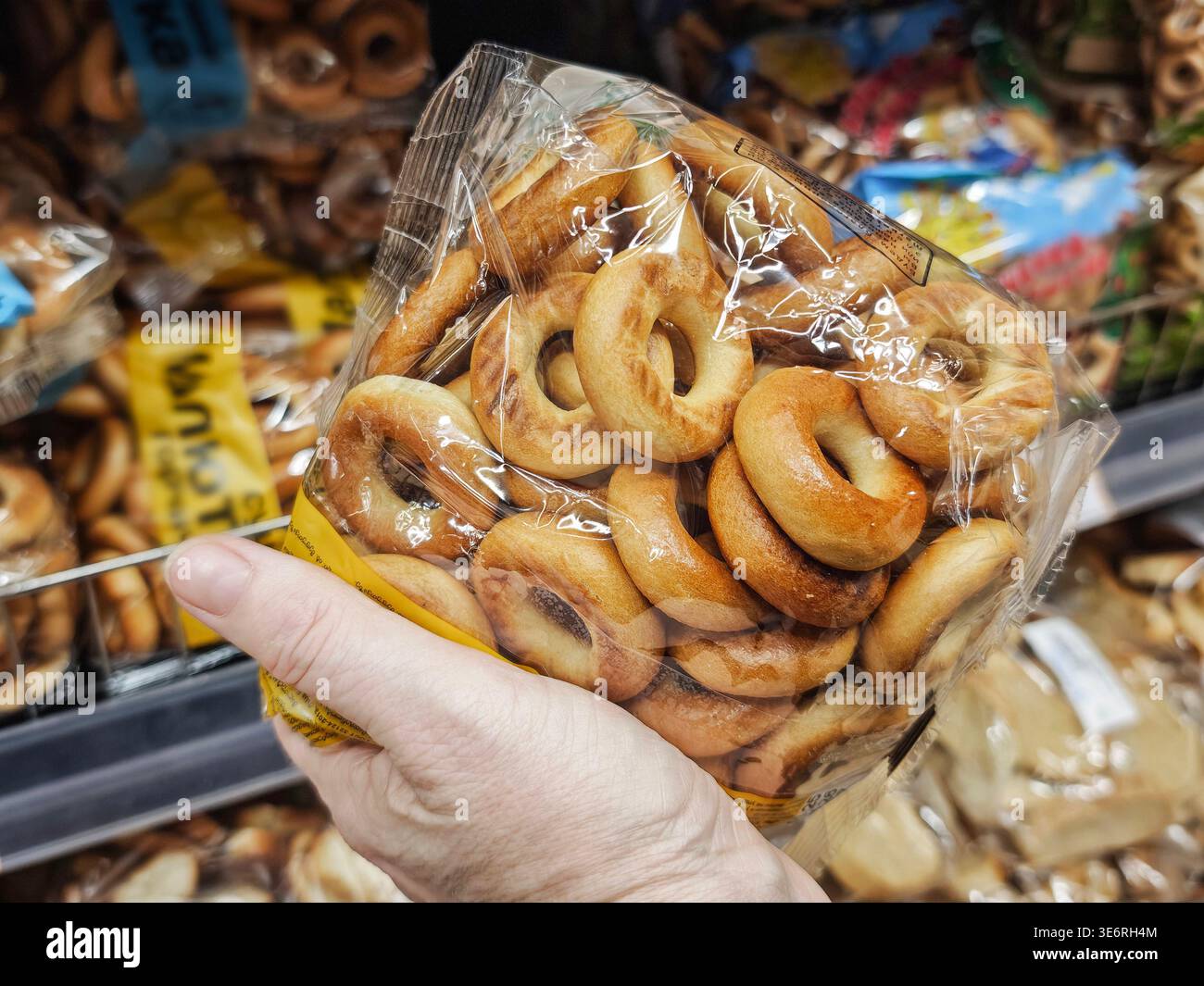 Una mano tiene in mano un sacchetto di bagel in un negozio di alimentari mentre seleziona gli articoli alimentari dagli scaffali durante un viaggio di shopping. Foto Stock