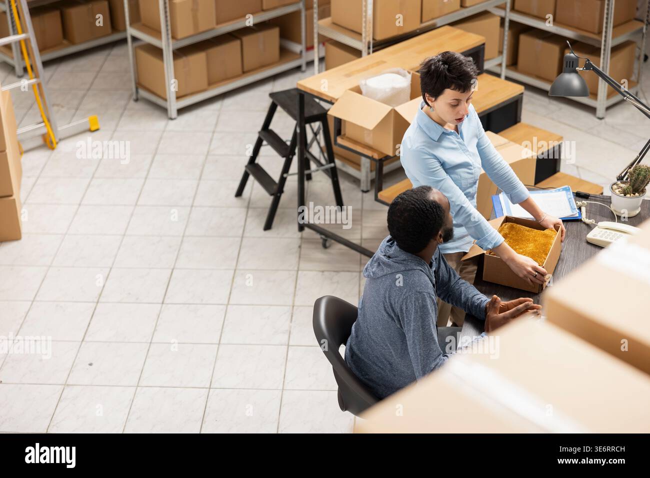 Team diversificato che supervisiona l'imballaggio e la consegna locale delle merci in un magazzino pieno di scatole e merci, mostrando le operazioni delle piccole imprese per la logistica degli ordini personalizzati. Commercio elettronico. Foto Stock