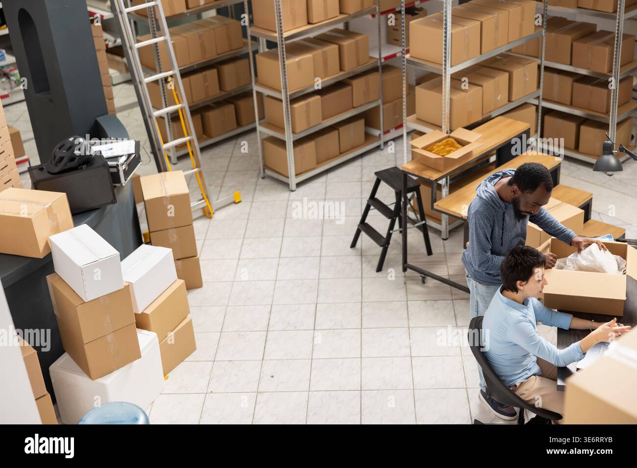 Personale diversificato che supervisiona l'imballaggio e la consegna locale delle merci in un magazzino pieno di scatole e merci, mostrando le operazioni delle piccole imprese per la logistica degli ordini personalizzati. Commercio elettronico. Foto Stock