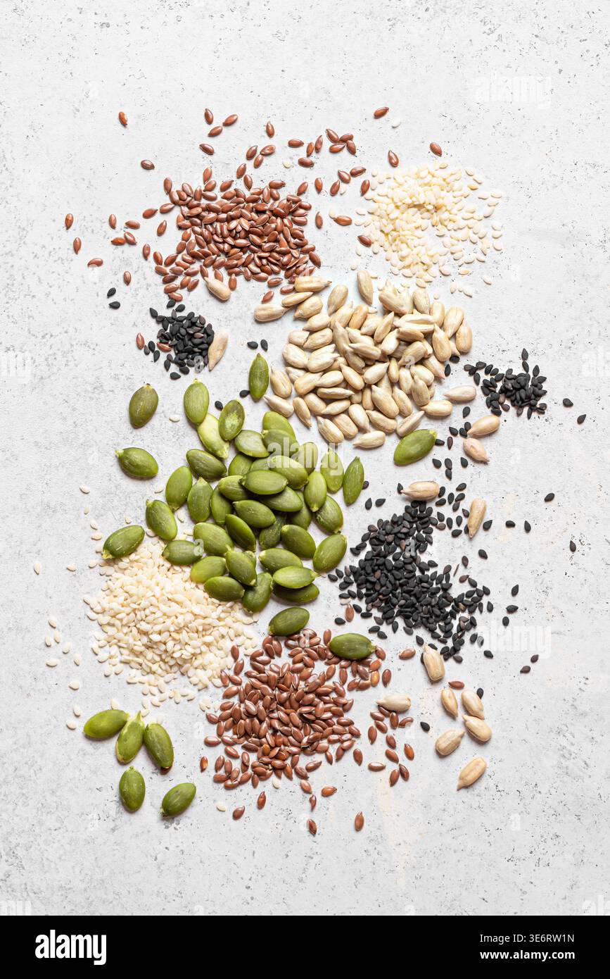 Miscela di semi su sfondo bianco, vista dall'alto, texture. Consistenza sana degli ingredienti alimentari. Semi di zucca, sesamo bianco e nero, chia, semi di girasole Foto Stock