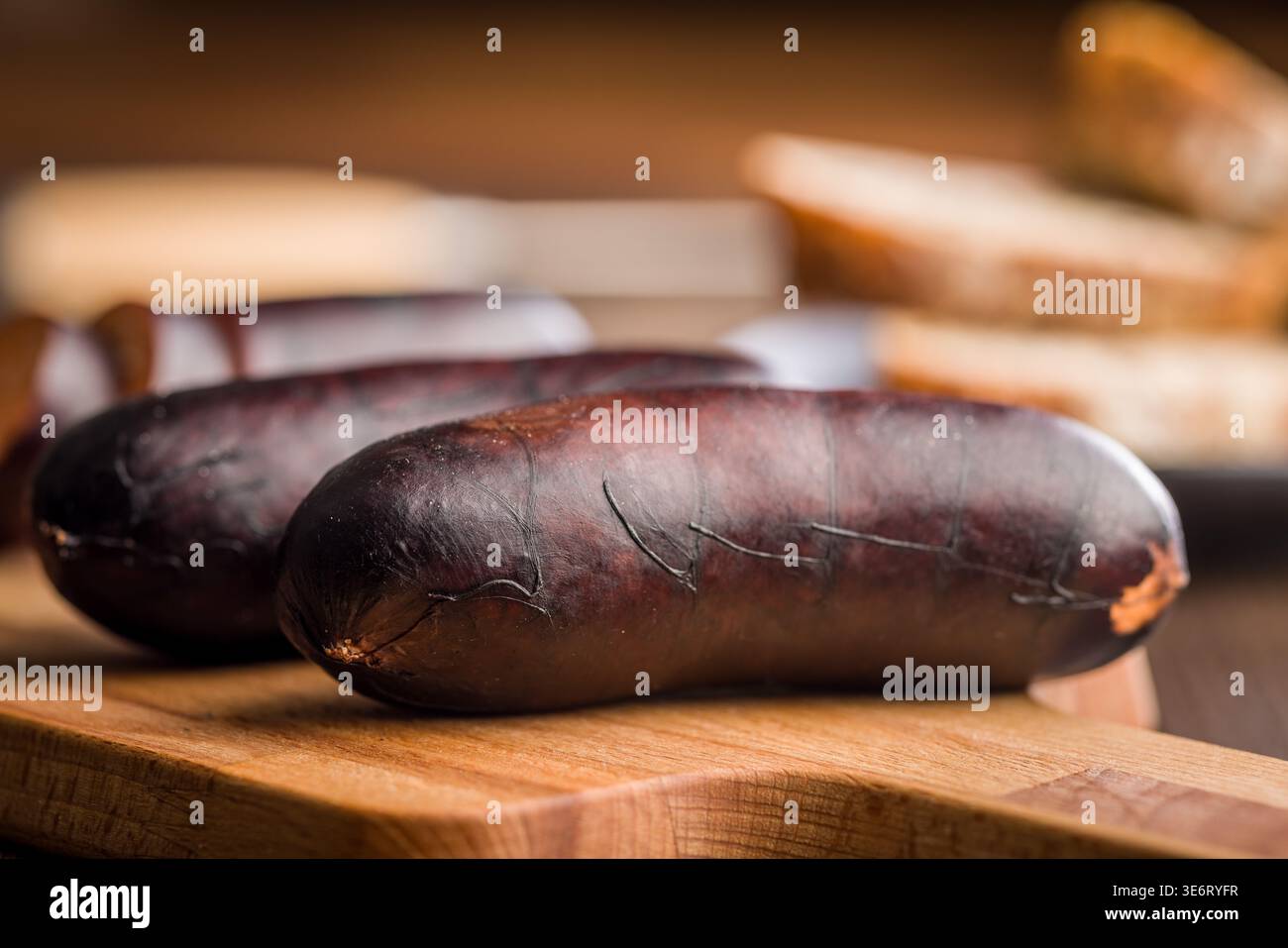 La salsiccia di sangue affumicata, chiamata anche budino nero, si trova su un tagliere di legno con pane affettato offuscato dietro di esso, evocando rustico, saporito e mestiere Foto Stock