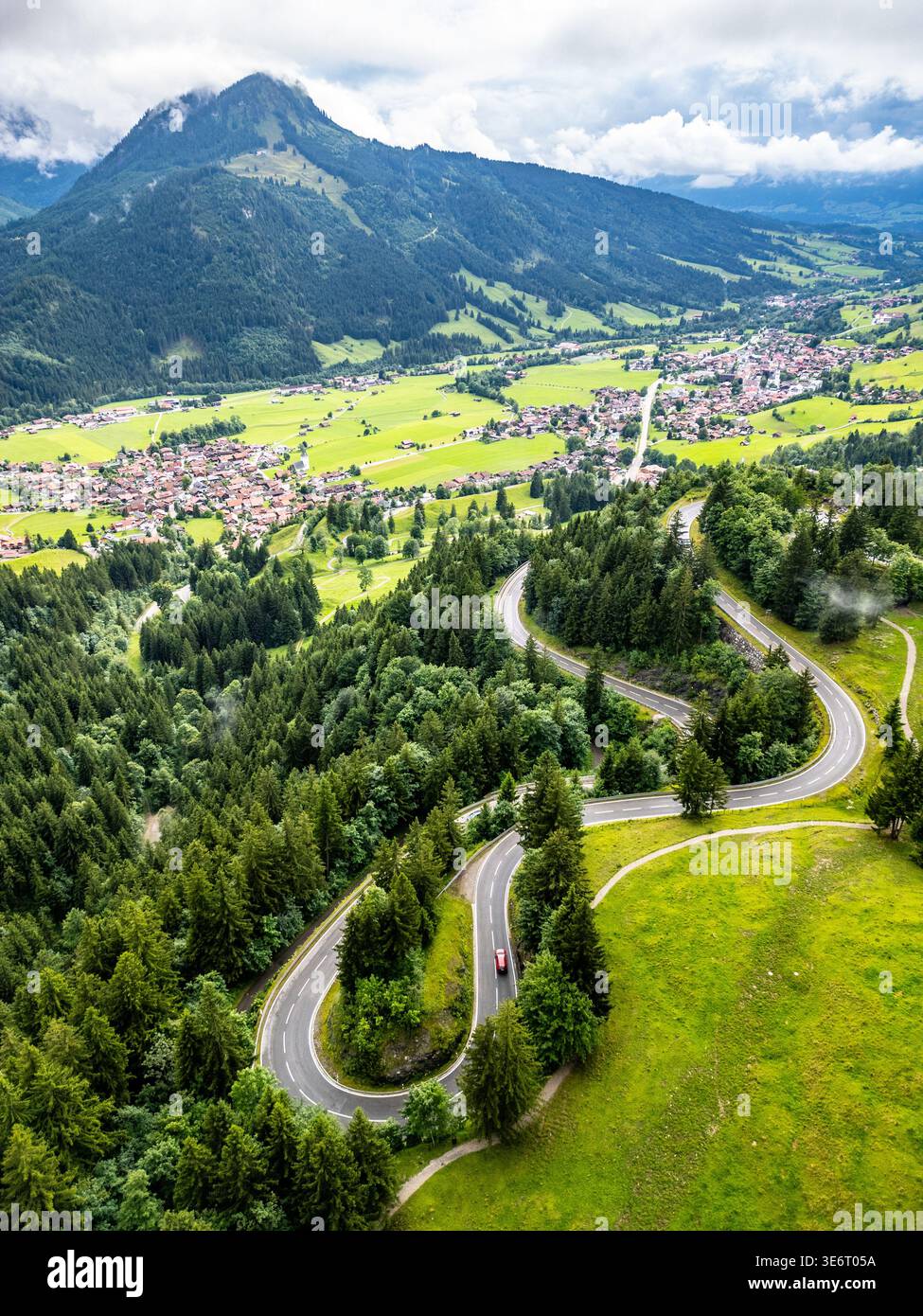 Una splendida vista aerea cattura le tortuose strade serpentine delle Alpi, circondate da lussureggianti colline verdi e vette montane. Ideale per gli amanti dell'avventura e dei viaggi su strada. Foto Stock