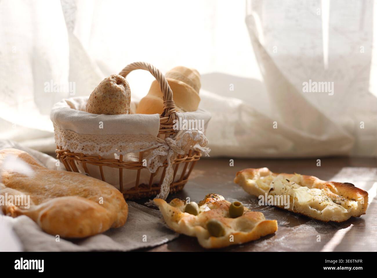 Focaccia italiana assortita e panini di pane fresco in cestino di vimini sul tavolo. La dose a livello di occhi è composta da focaccine tradizionali con olive e cipolle Foto Stock