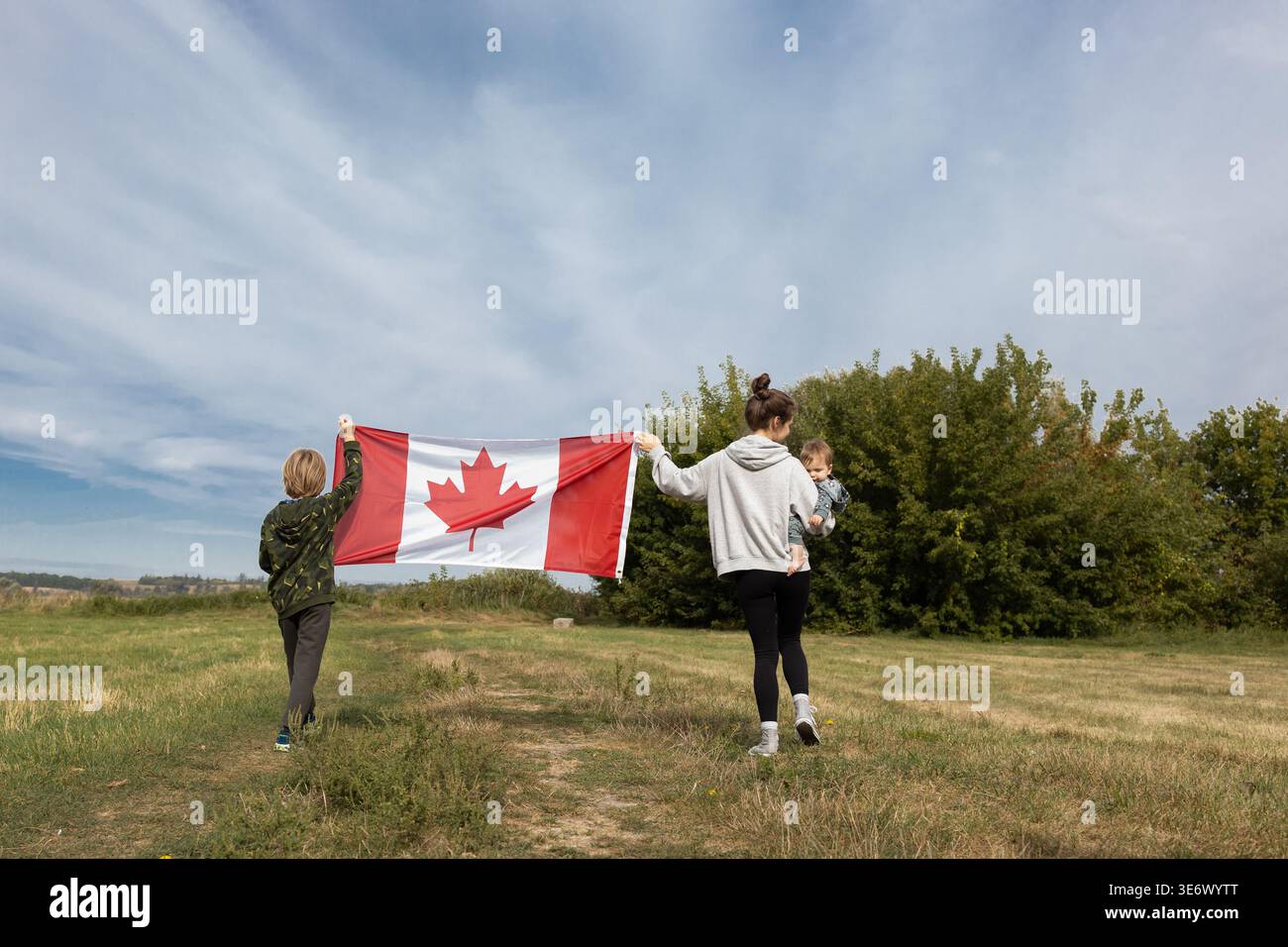 Bandiera canadese detenuta da persone che camminano nella natura. Buon Canada Day. Orgoglio, libertà, patriottismo. Viaggiando attraverso il paese. Simbolo nazionale. Mamma con Foto Stock