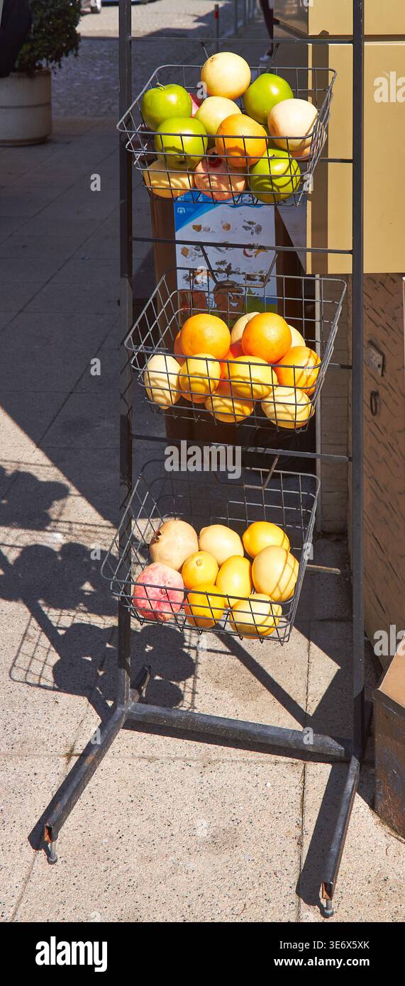 Lo stand di frutta a filo presenta mele verdi, arance e limoni in tre cestini, posizionati all'esterno di un mercato con un cielo azzurro cristallino sullo sfondo Foto Stock