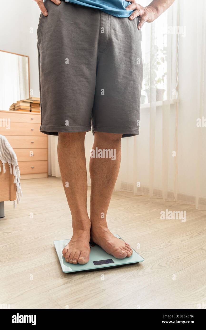 Uomo in piedi su una bilancia digitale in camera da letto, a controllare il peso. Concetti di dieta, fitness, salute, e viaggio di perdita di peso Foto Stock