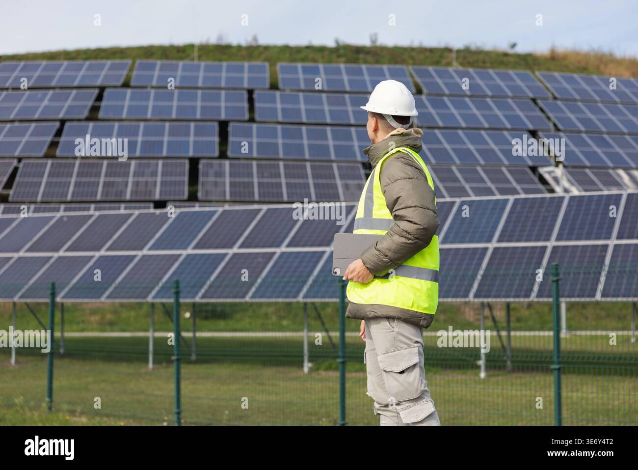 Un giovane ingegnere elettrico maschio ispeziona i sistemi a pannelli solari e gestisce le installazioni utilizzando un computer portatile in un'area di energia rinnovabile. Foto Stock