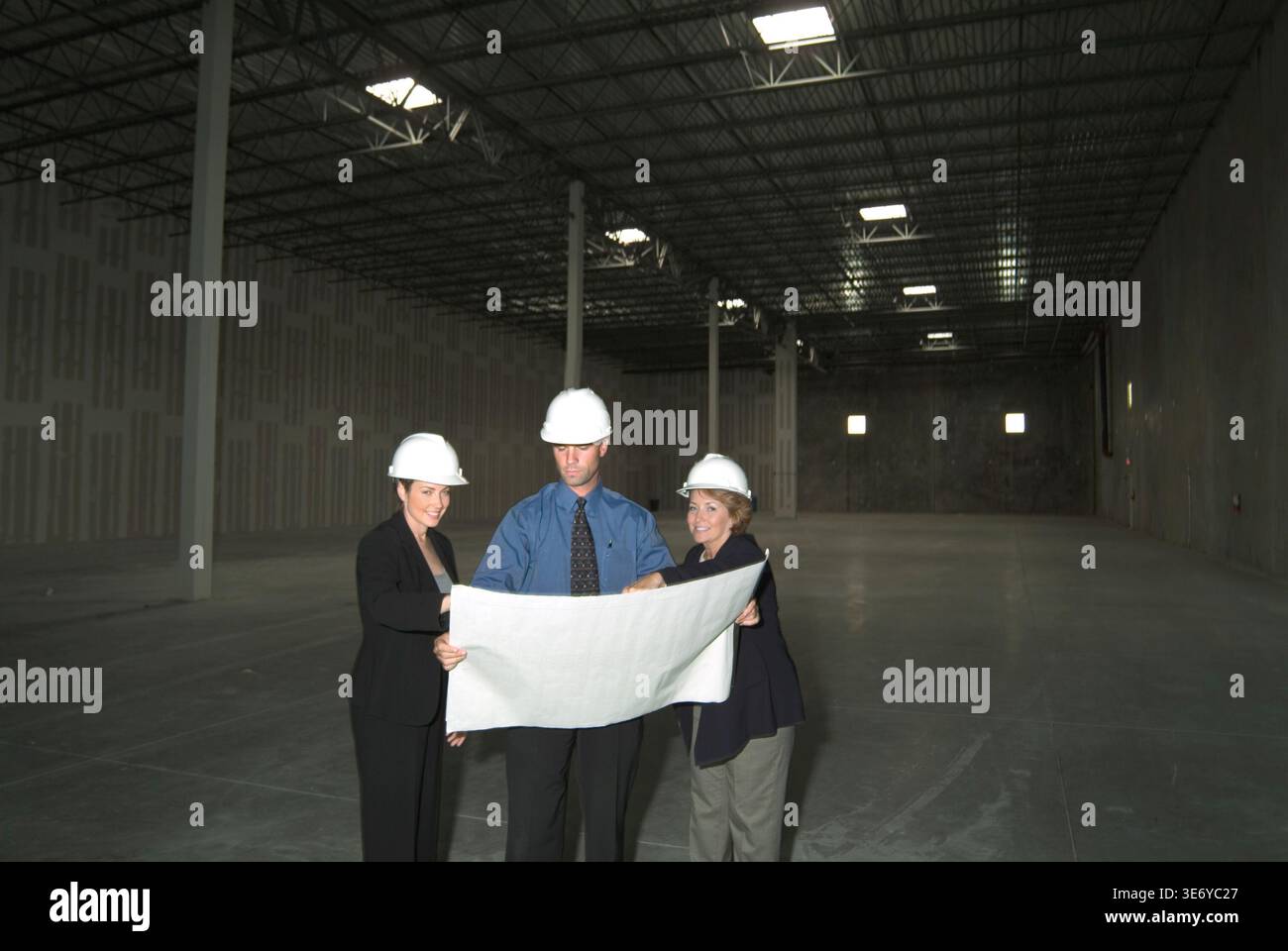 Rappresentanti aziendali che esaminano i progetti con un ingegnere edile all'interno di un nuovo magazzino vuoto, New Jersey USA Foto Stock
