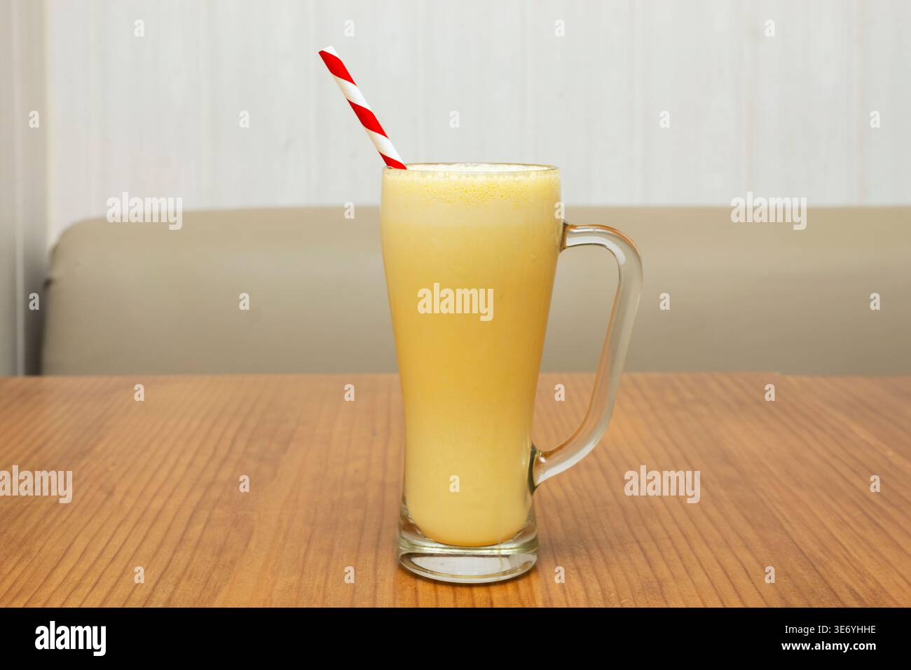 Un bicchiere alto e lucido che trabocca di succo d'arancia fresco, che rivela piccole bollicine e polpa fluttuante alla luce del mattino Foto Stock
