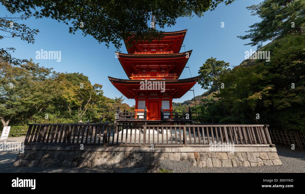 Kyoto, Giappone - 16 ottobre 2023: La pagoda Koyasu a tre piani, dipinta in rosso e bianco, è vista da un angolo frontale diretto all'interno del tempio Kiyomizu-dera, circondata da alberi e racchiusa da una recinzione di legno sotto un cielo azzurro. Foto Stock