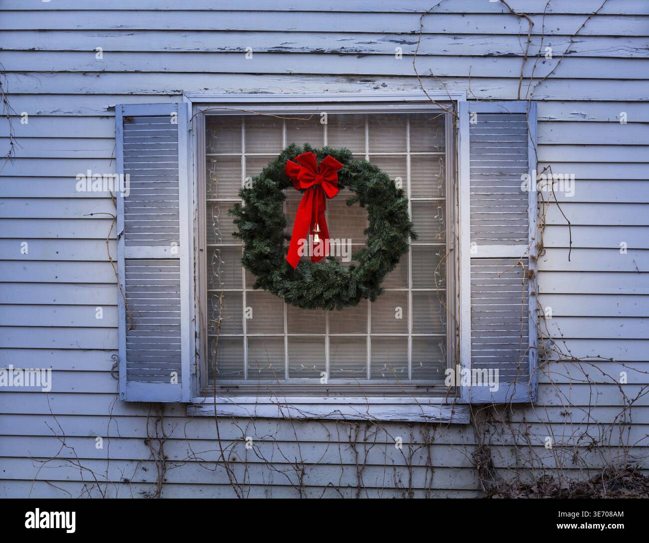 Design tradizionale di una corona natalizia attaccata alla finestra di una vecchia casa e decaduta con vernice che sbucciava Foto Stock
