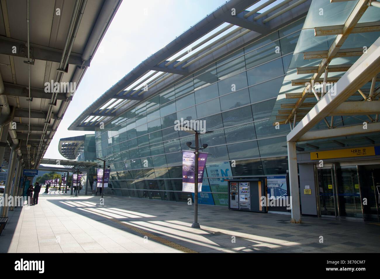 La facciata in vetro della stazione di Ulsan è un passaggio pedonale coperto con porte d'ingresso, lampioni e lunghe ombre all'esterno del terminal KTX. Foto Stock