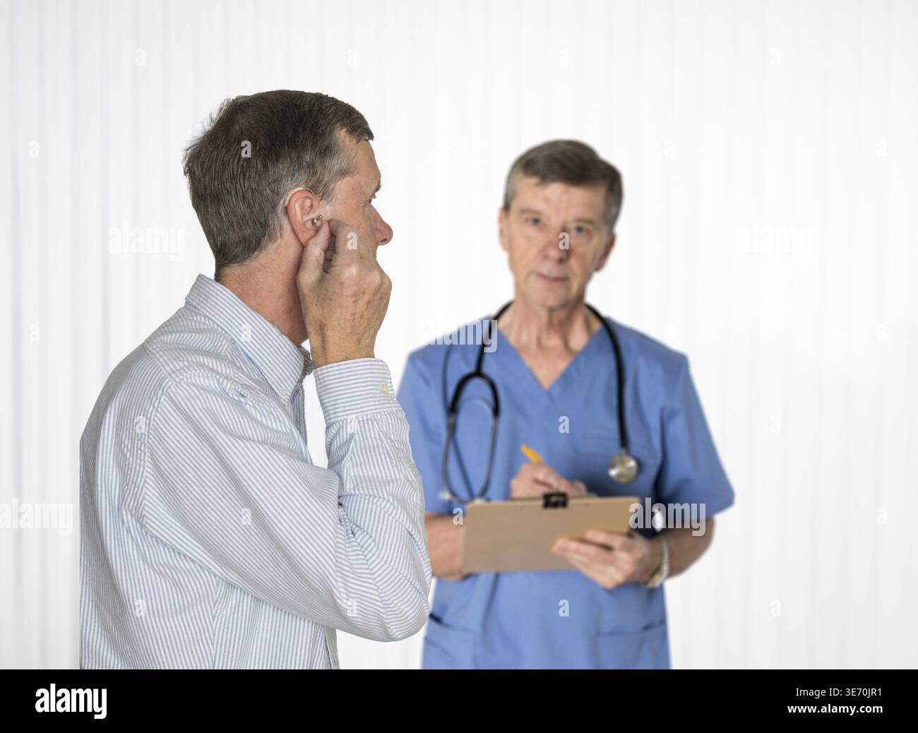 Maschio anziano che inserisce l'apparecchio acustico nell'orecchio in consultazione con il suo audiologo Foto Stock
