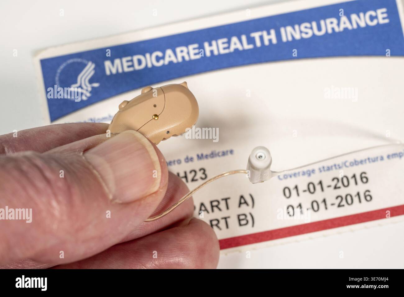 Macro primo piano delle dita che tengono piccoli apparecchi acustici moderni sullo sfondo della scheda medicare come la copertura sanitaria è migliorata Foto Stock