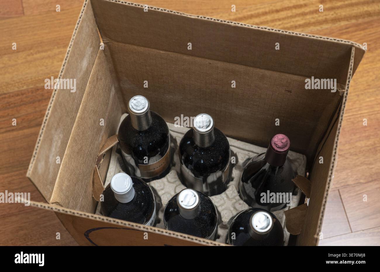 Aprire la scatola di una mezza dozzina di bottiglie di vino per la consegna a casa seduta su pavimento in legno Foto Stock