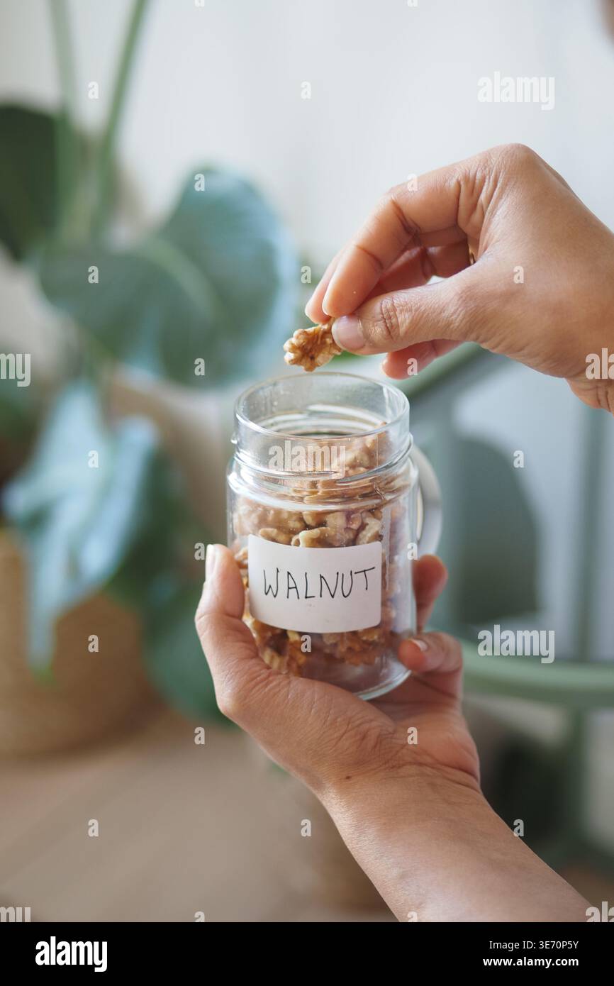Mani che tengono il vaso di noci in cucina Foto Stock