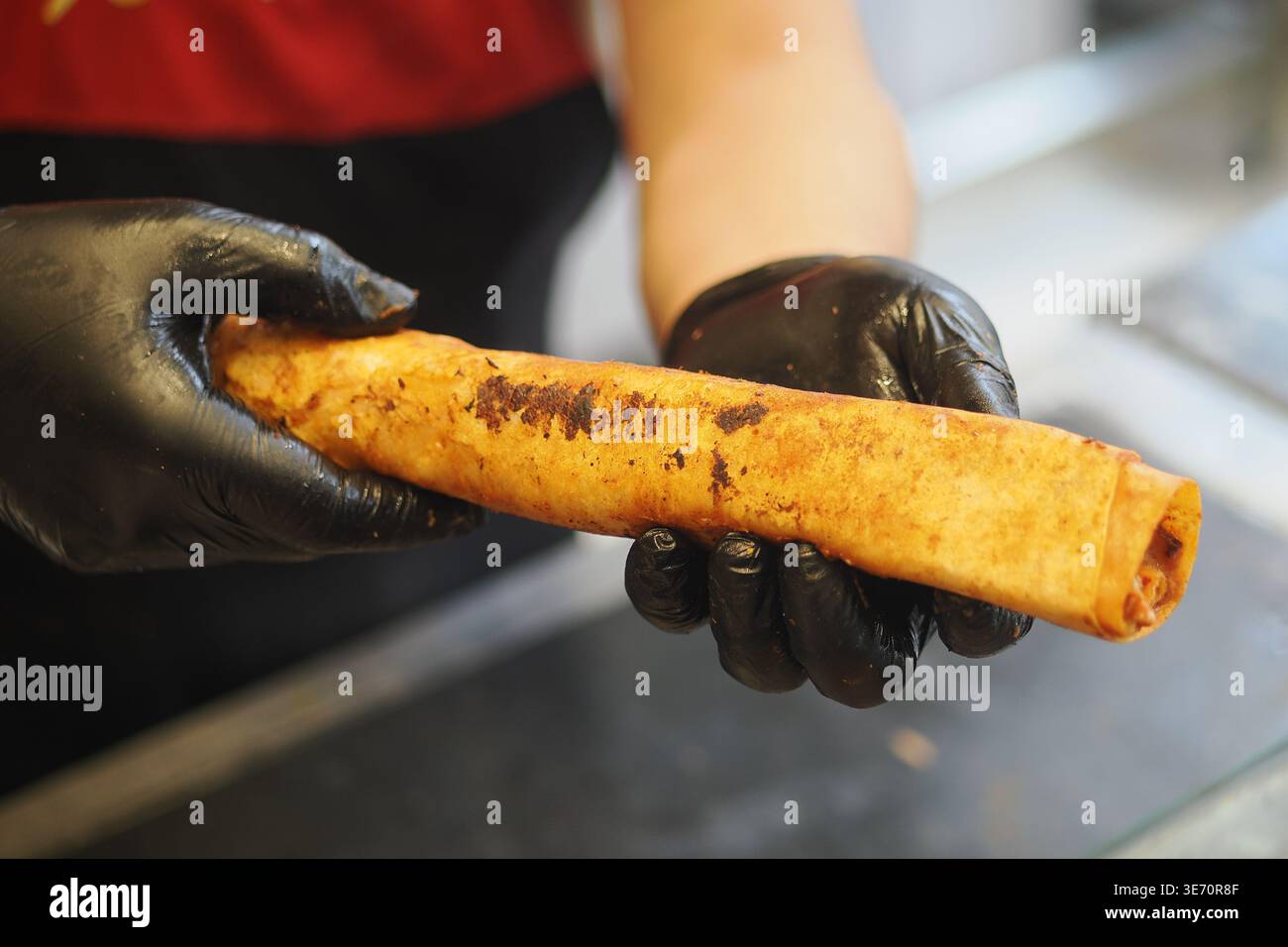 Il venditore di alimenti tiene un piatto arrotolato preparato in cucina Foto Stock