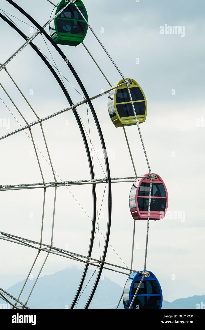 Le colorate gondole della ruota panoramica si affacciano su un cielo nuvoloso, mettendo in risalto la struttura geometrica e il design vivace. Foto Stock