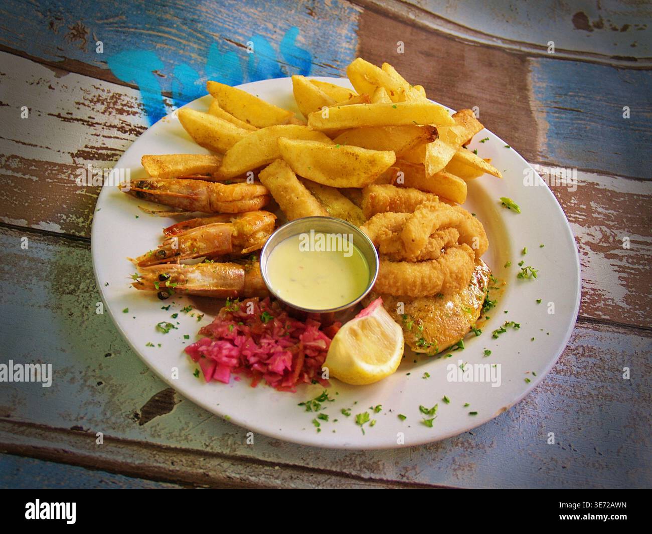 Piatto di pesce con gamberi, calamari e patatine fritte su un tavolo di legno rustico Foto Stock